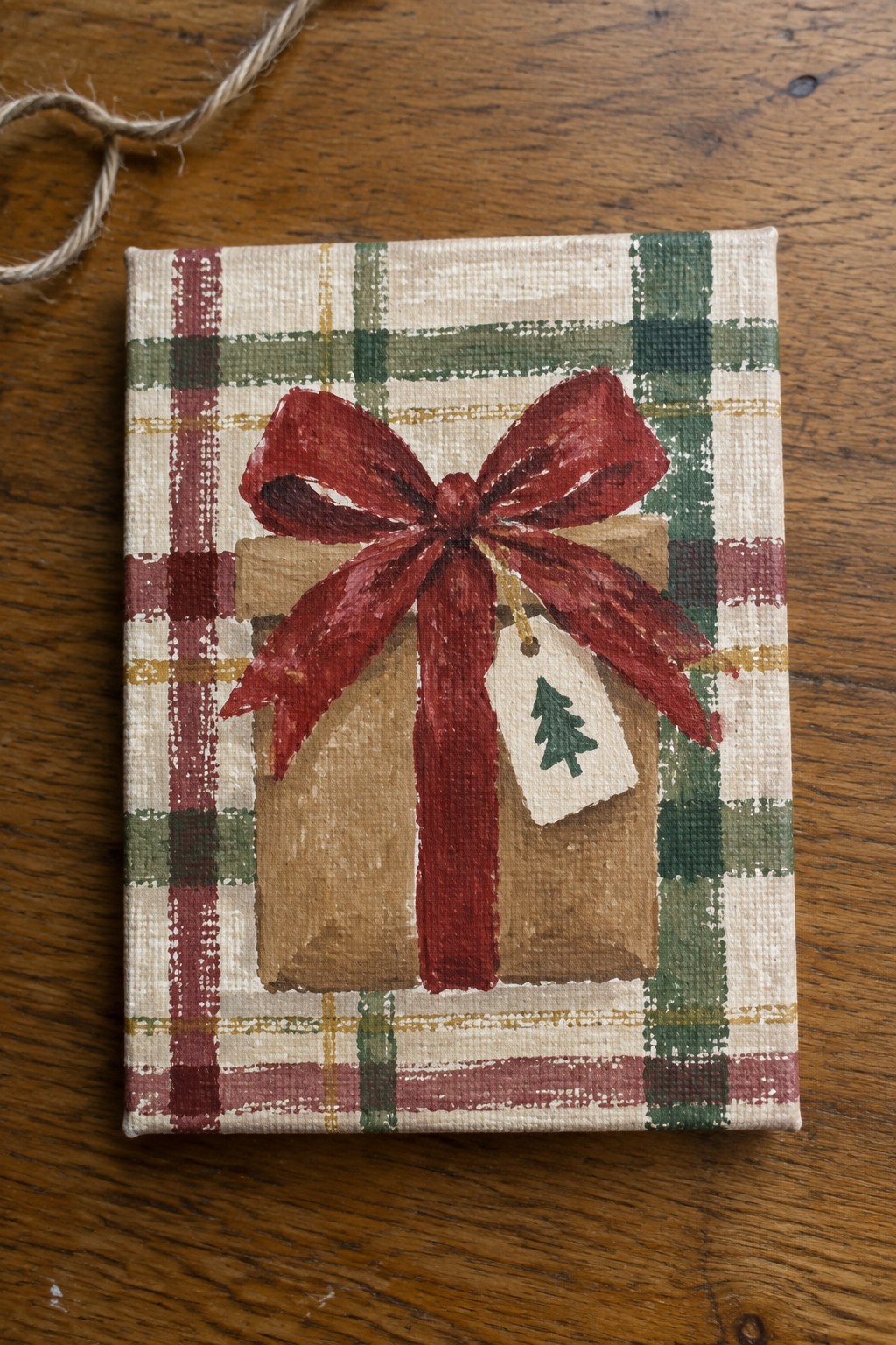 Canvas painting of brown gift with red bow and tree tag on plaid background