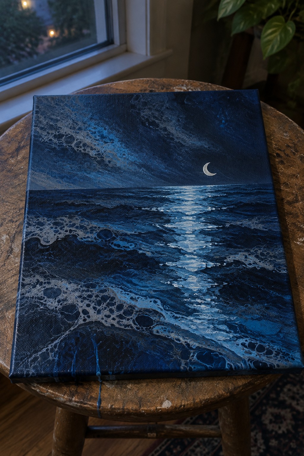 Blue fluid art seascape with crescent moon on wooden stool by window
