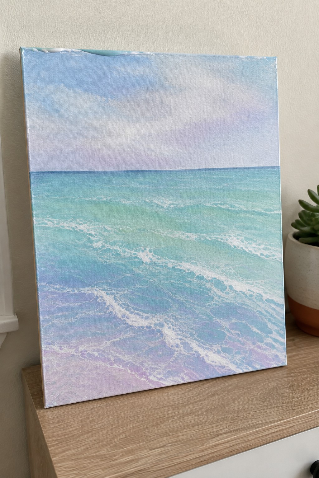 Seascape painting of turquoise waves with white foam on wooden surface beside plant