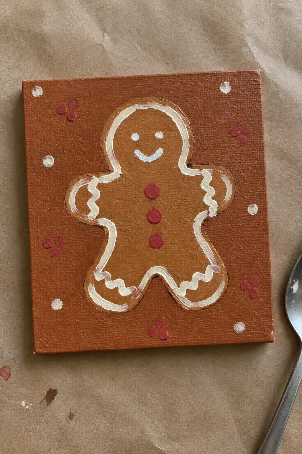 Gingerbread man painting with white icing outline and red buttons on orange canvas