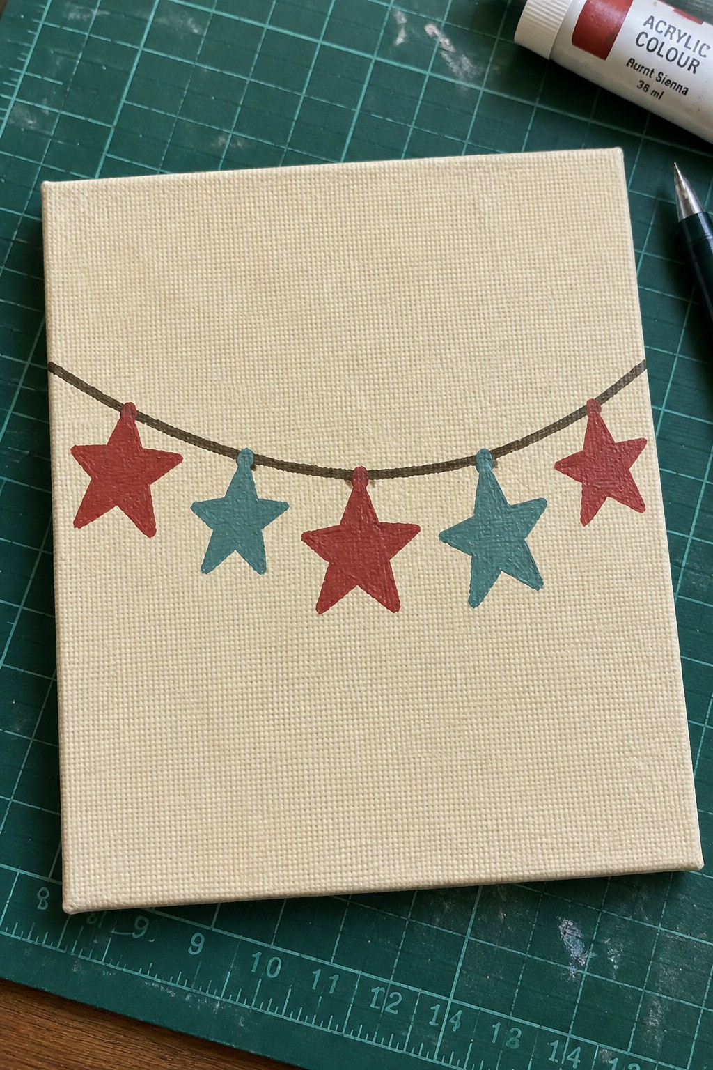 Canvas with red and teal stars strung on brown line over green cutting mat