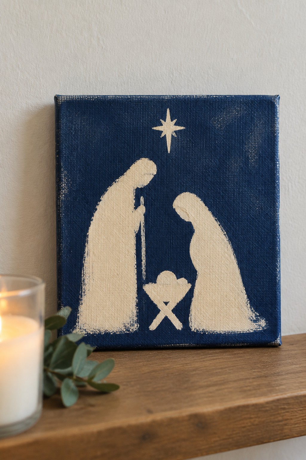 Minimalist cream nativity figures and star on dark blue canvas beside candle
