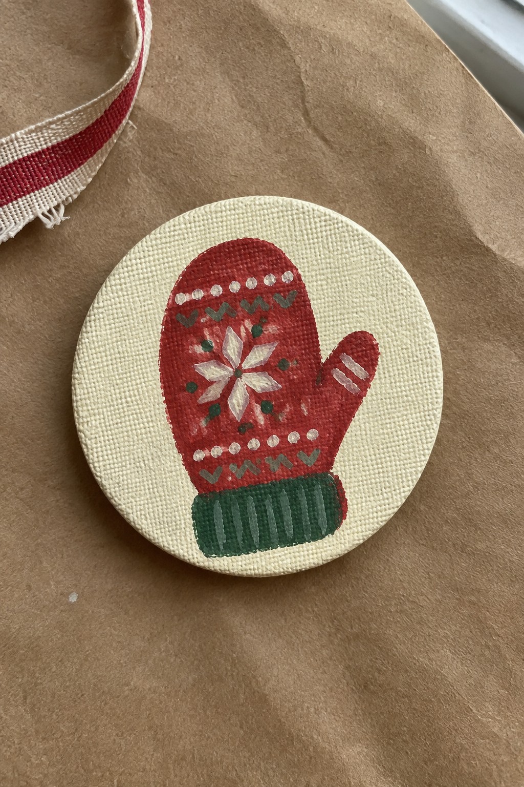 Red mitten with snowflake on round canvas beside striped ribbon