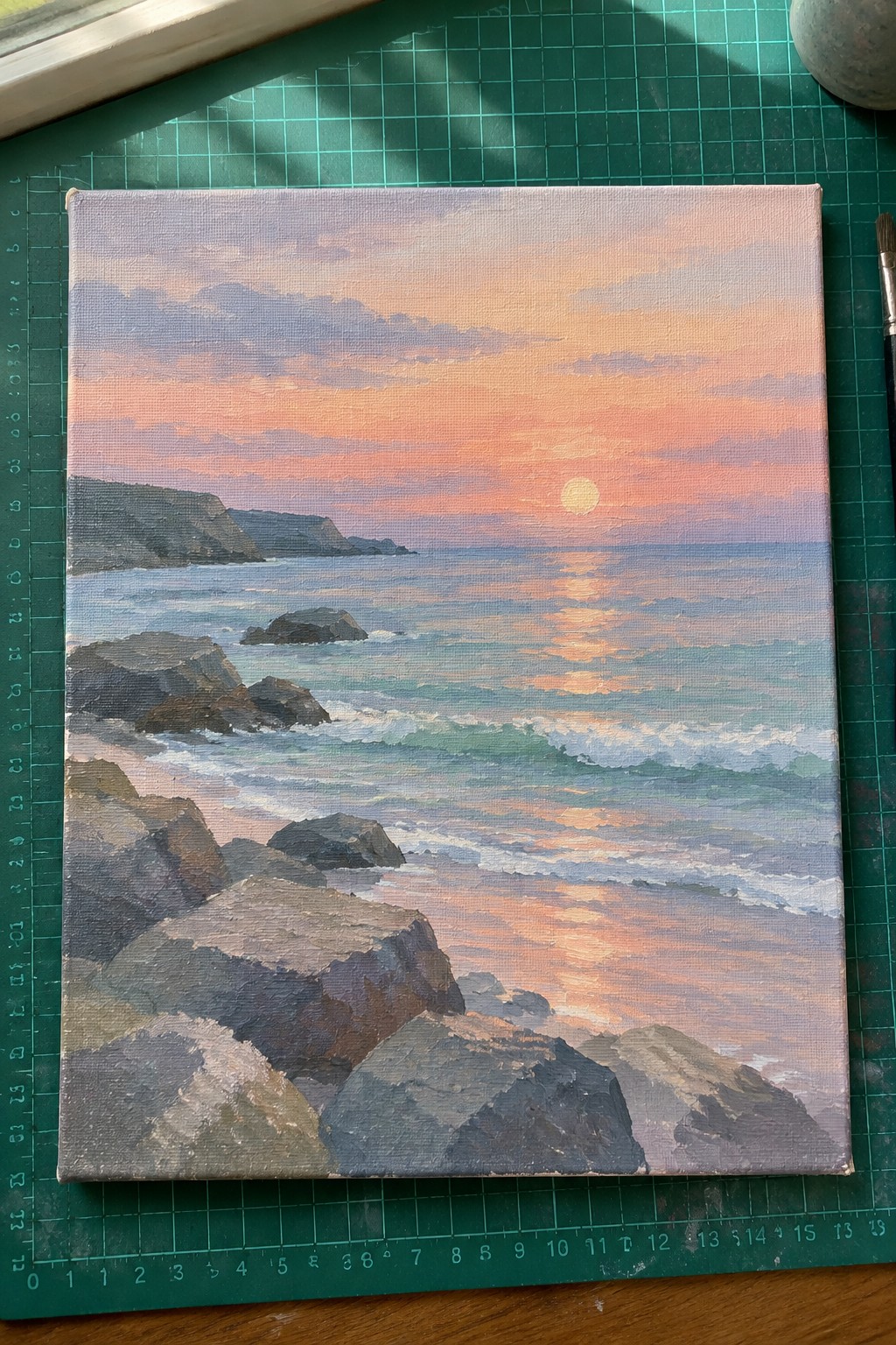 Seascape oil painting of sunset over rocky waves on green cutting mat