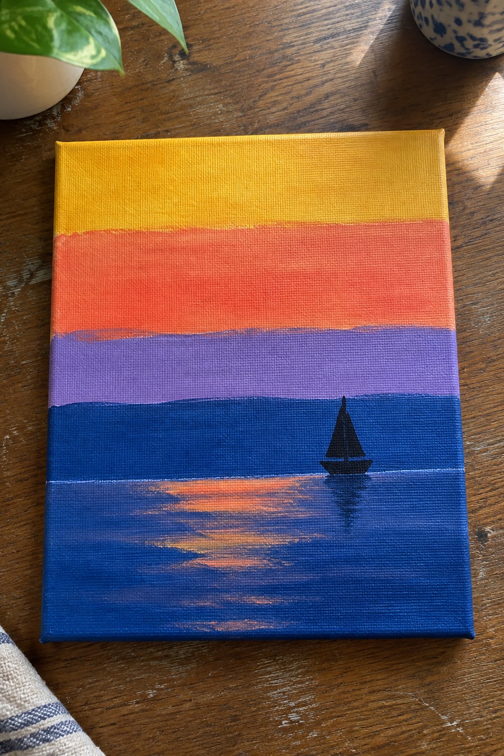 Colorful sunset canvas with yellow-orange-purple-blue stripes and black sailboat reflection