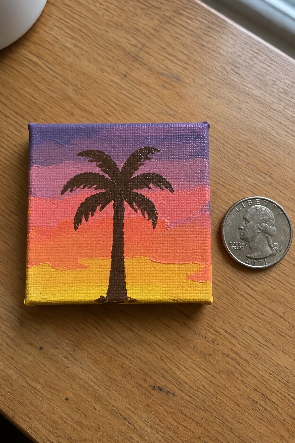 Miniature palm tree sunset painting on canvas beside a 2021 quarter for scale