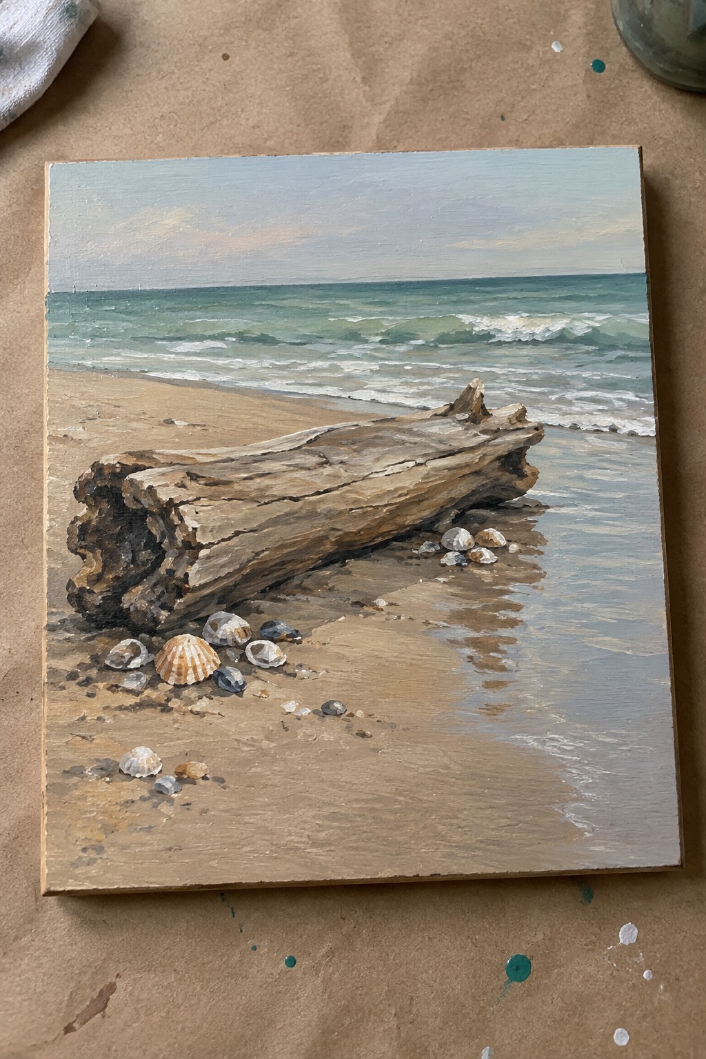Oil painting of driftwood log and seashells on sandy beach with ocean waves