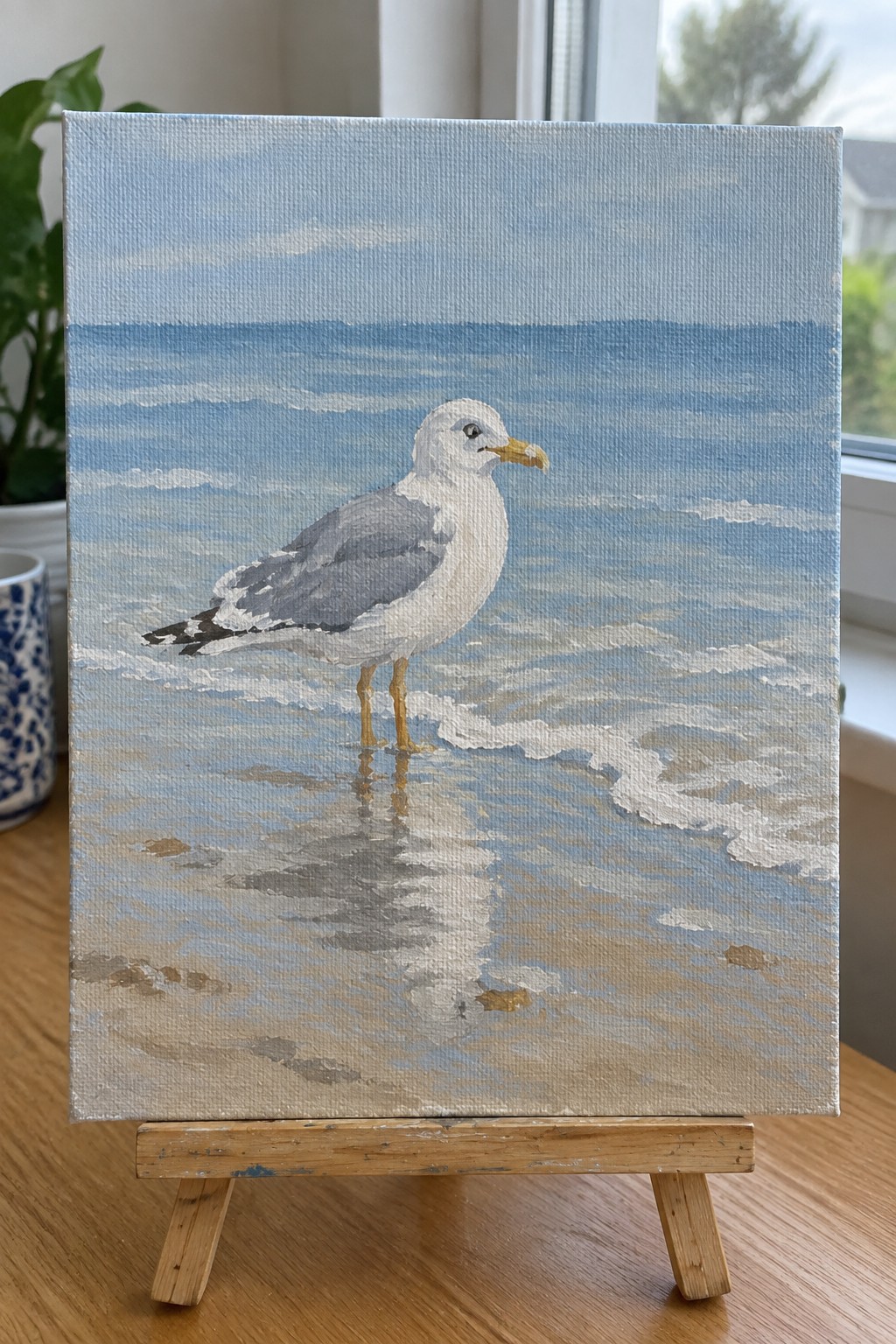 Painting of white seagull in shallow beach waves on wooden easel