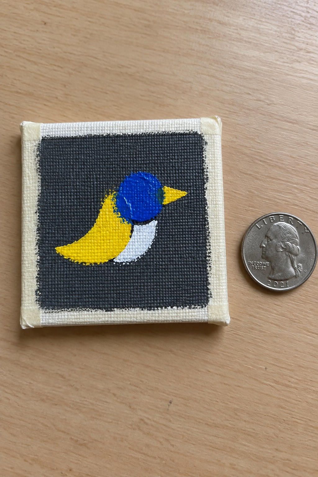 Tiny canvas painting of blue-yellow bird beside a 2021 quarter on wood