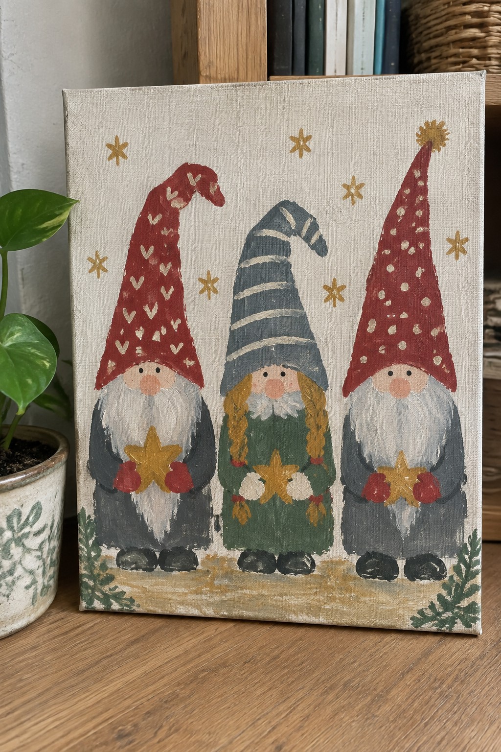 Three gnomes in tall patterned hats hold golden stars on canvas.
