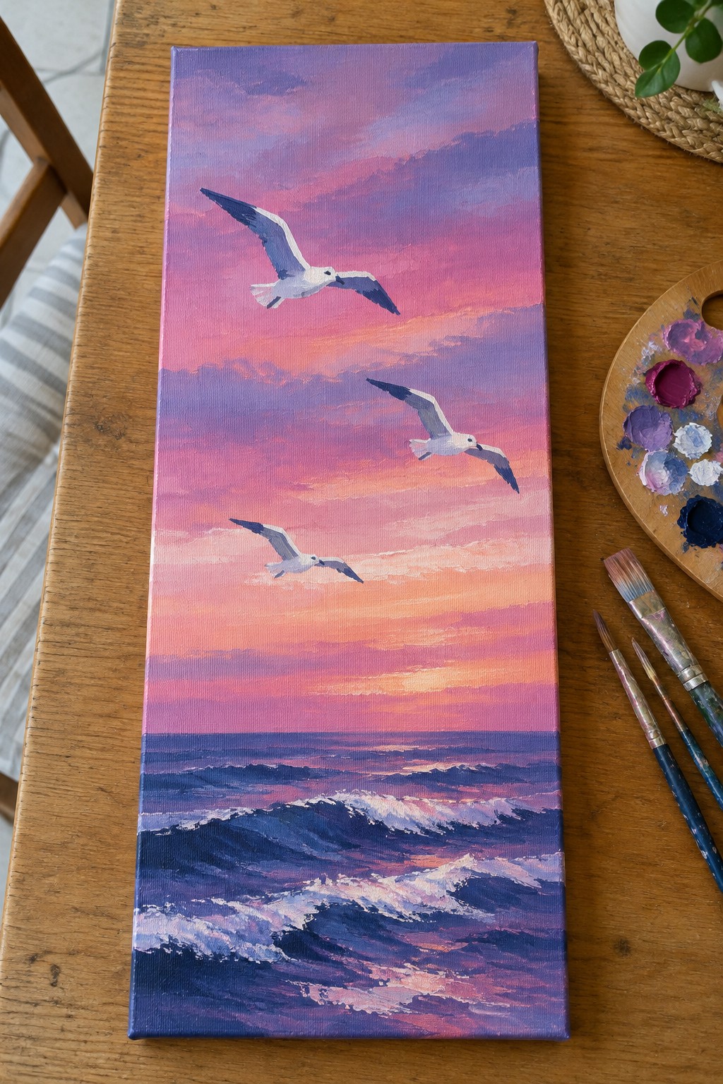 Painting of three seagulls flying over waves beneath pink-purple sunset sky with palette nearby