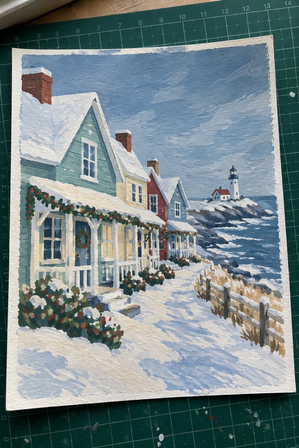 Snowy coastal village with colorful Christmas-decorated houses and distant lighthouse.