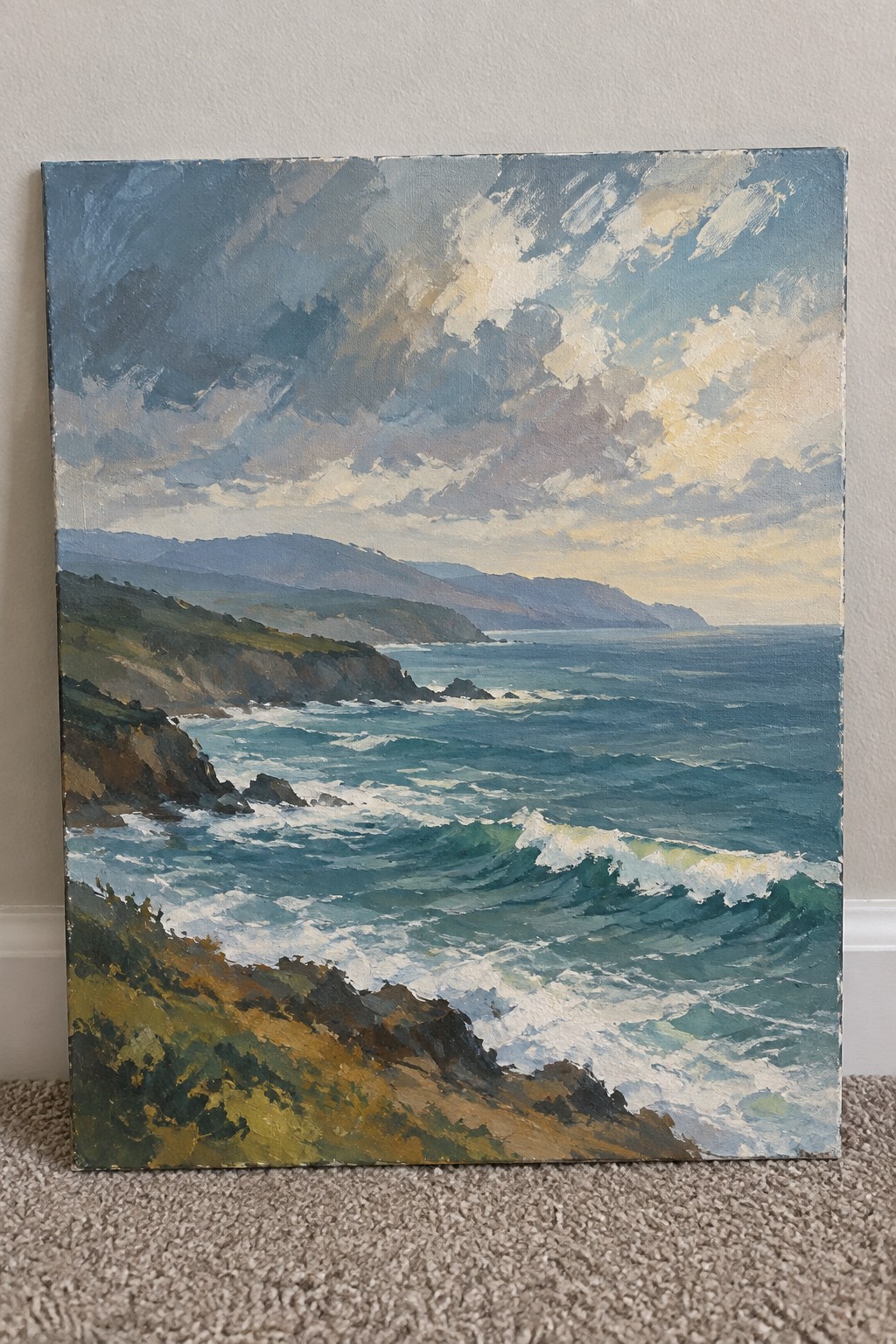 Painting of crashing waves on rocky cliffs with green hills under dramatic cloudy sky