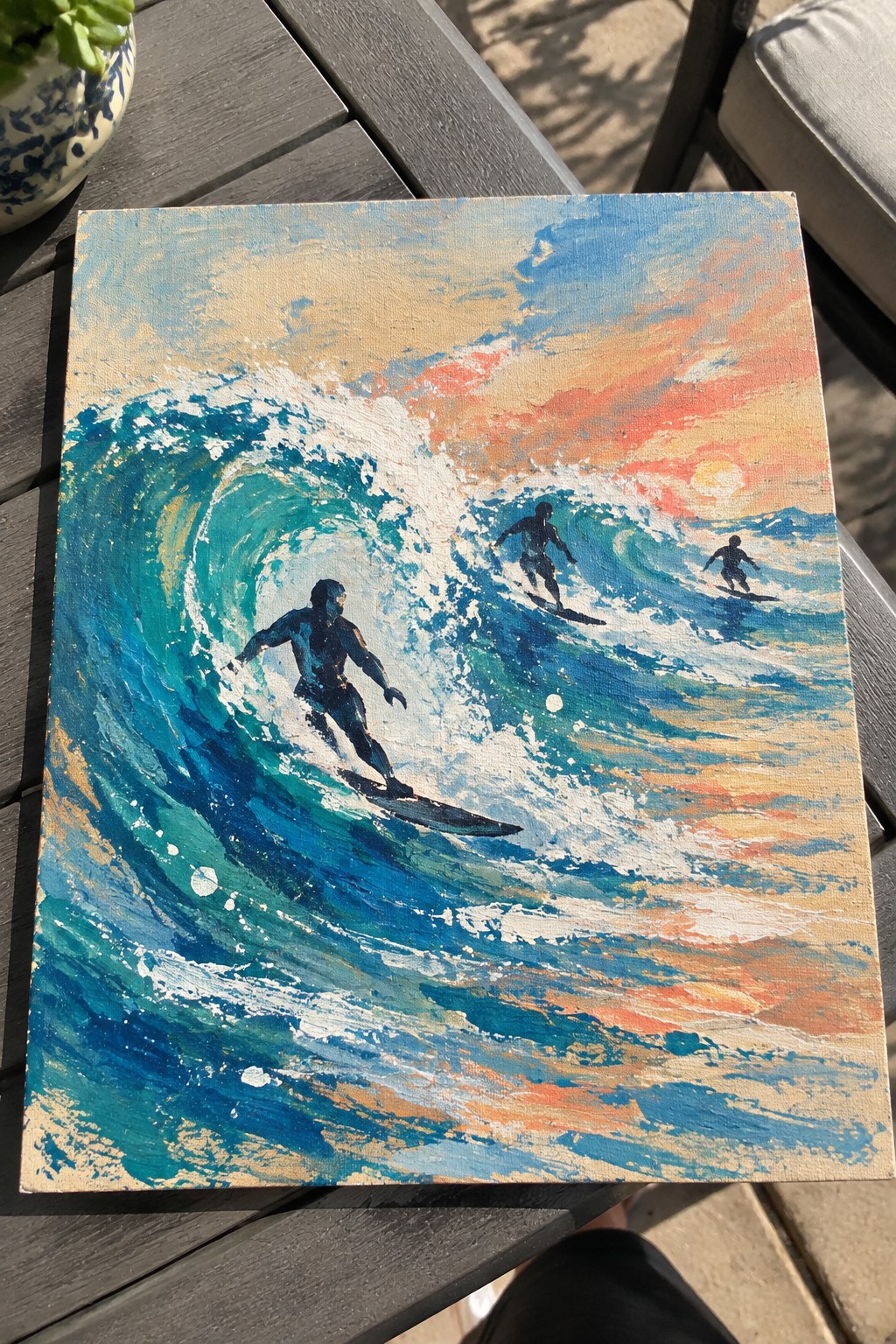 Canvas painting of three surfers on teal waves beneath orange sunset sky