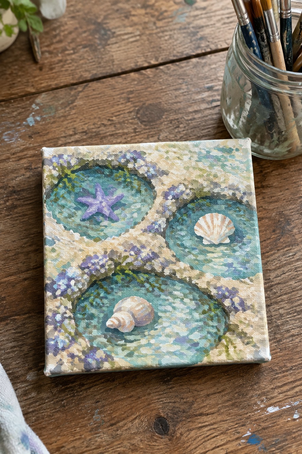 Small canvas painting of three tide pools with starfish, shell and conch on wood table