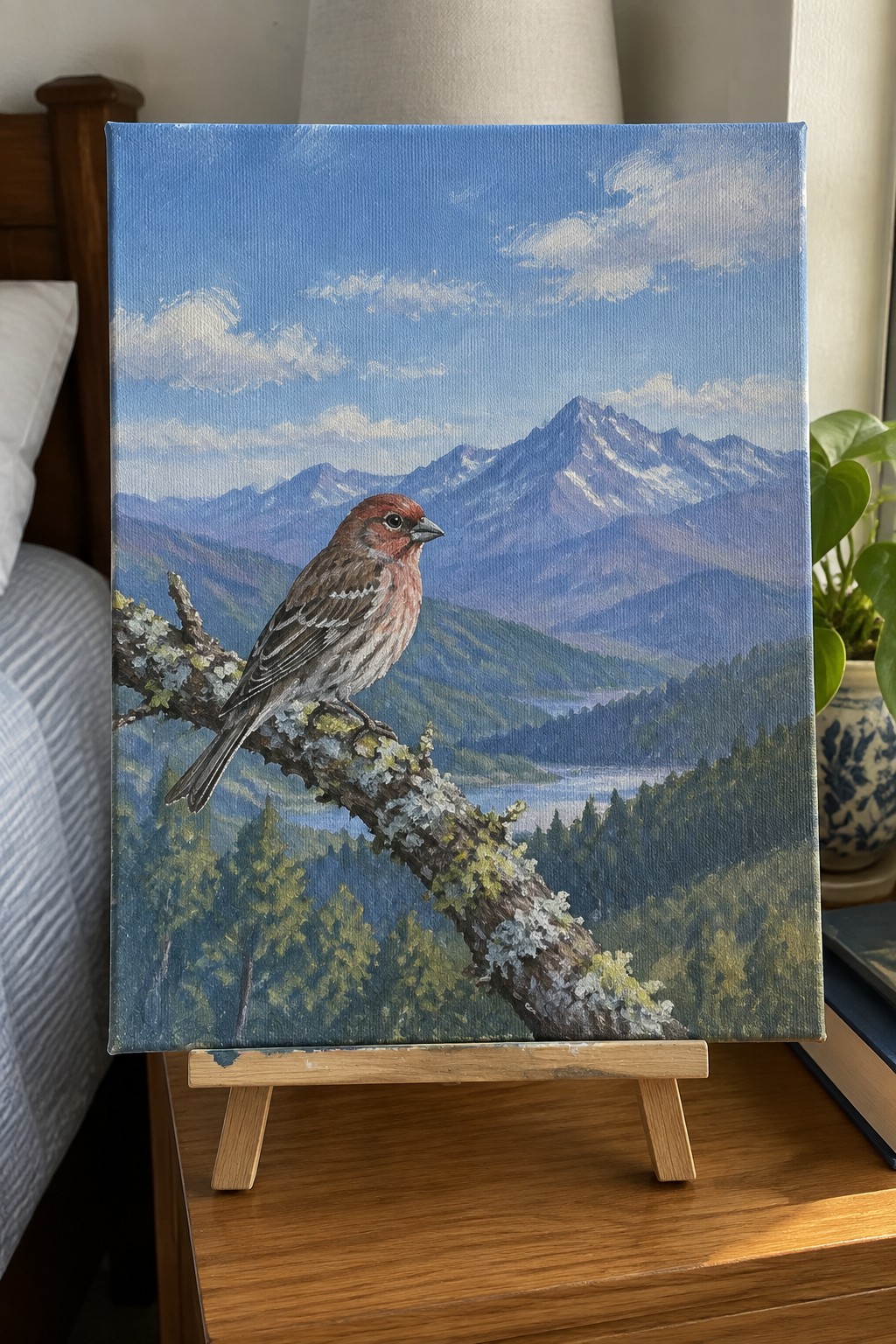 Realistic painting of reddish bird on branch overlooking forested mountain landscape on easel