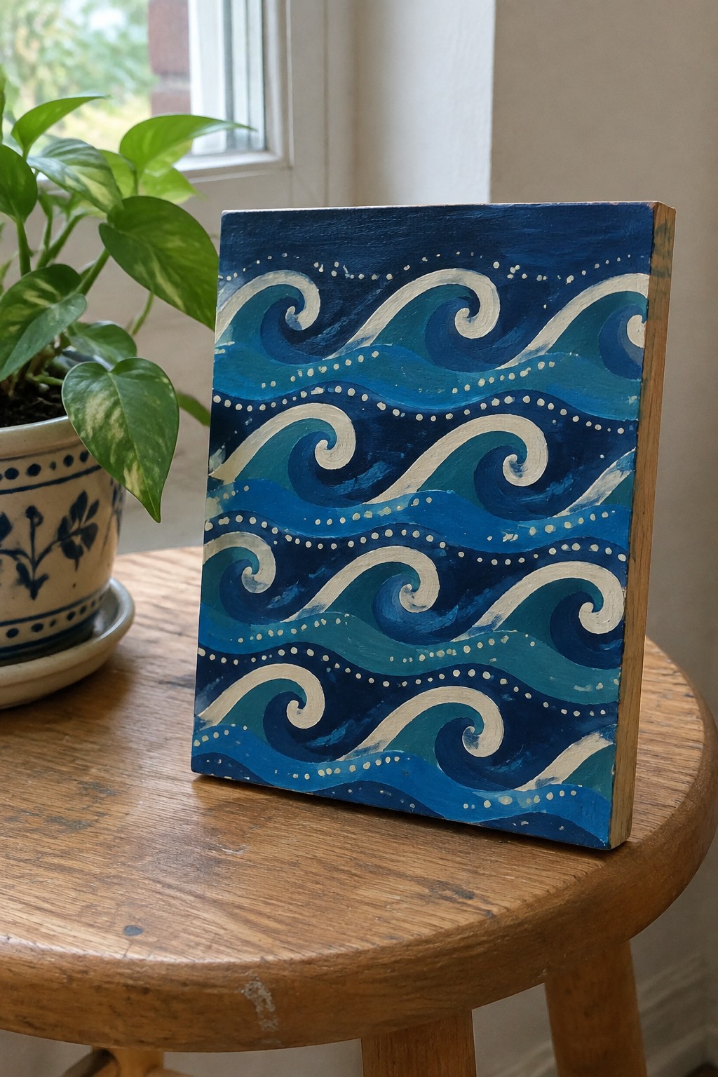Swirling blue wave painting on wooden table beside potted plant