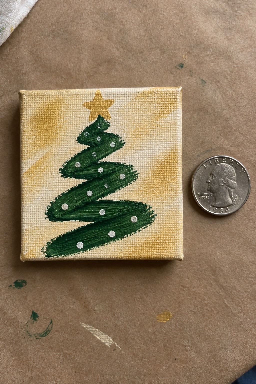 Small canvas with green Christmas tree, gold star, and white dots beside a quarter