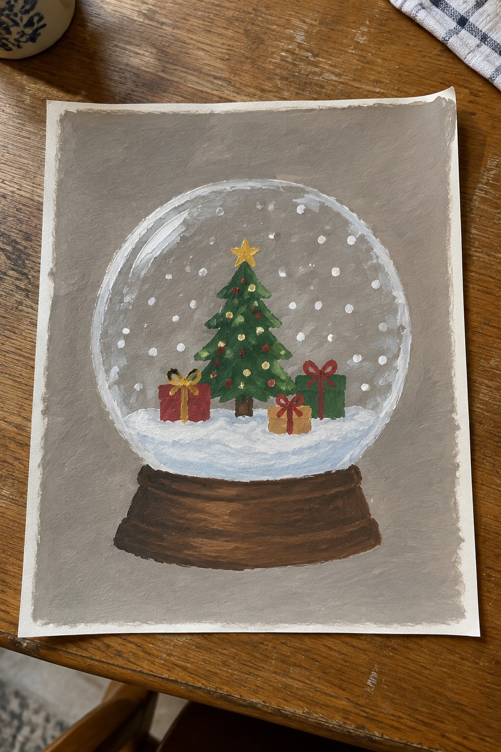 Acrylic painting of a snow globe with a decorated Christmas tree and four gift boxes inside, sitting on a wooden table.