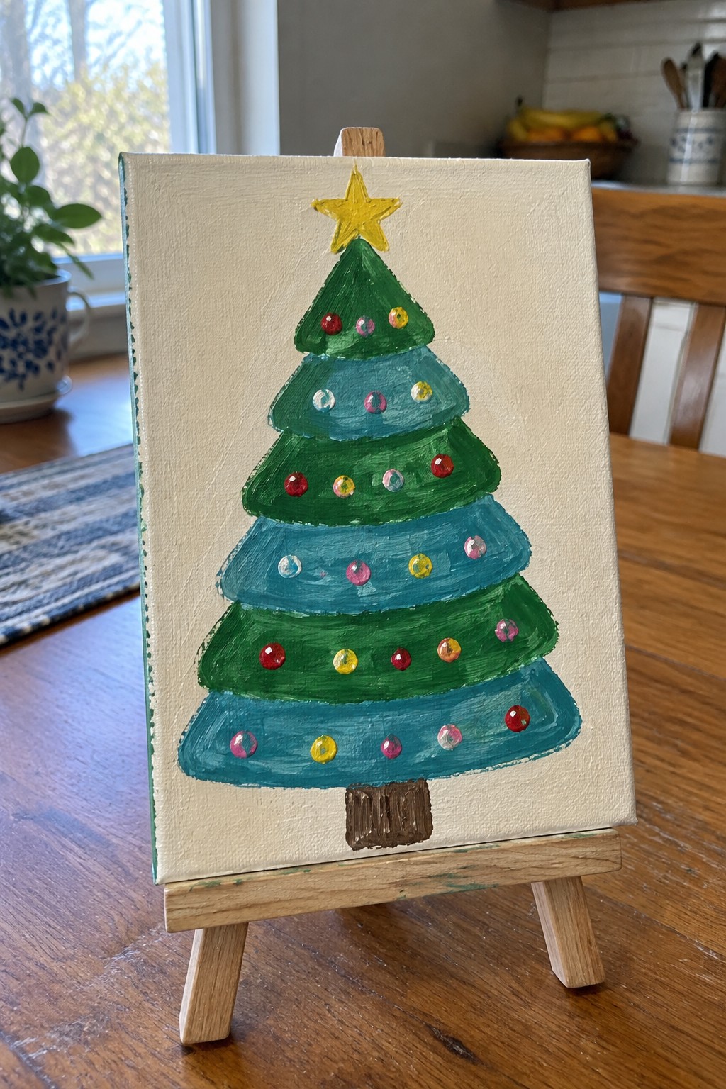 Layered green Christmas tree painting with star and ornaments on wooden easel.