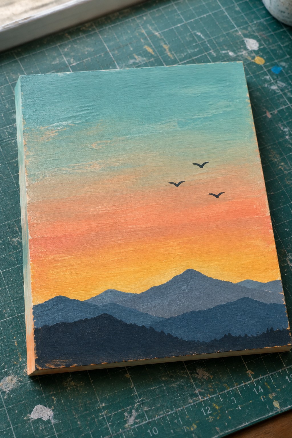Sunset gradient sky over dark mountain silhouettes with three birds on painted canvas.