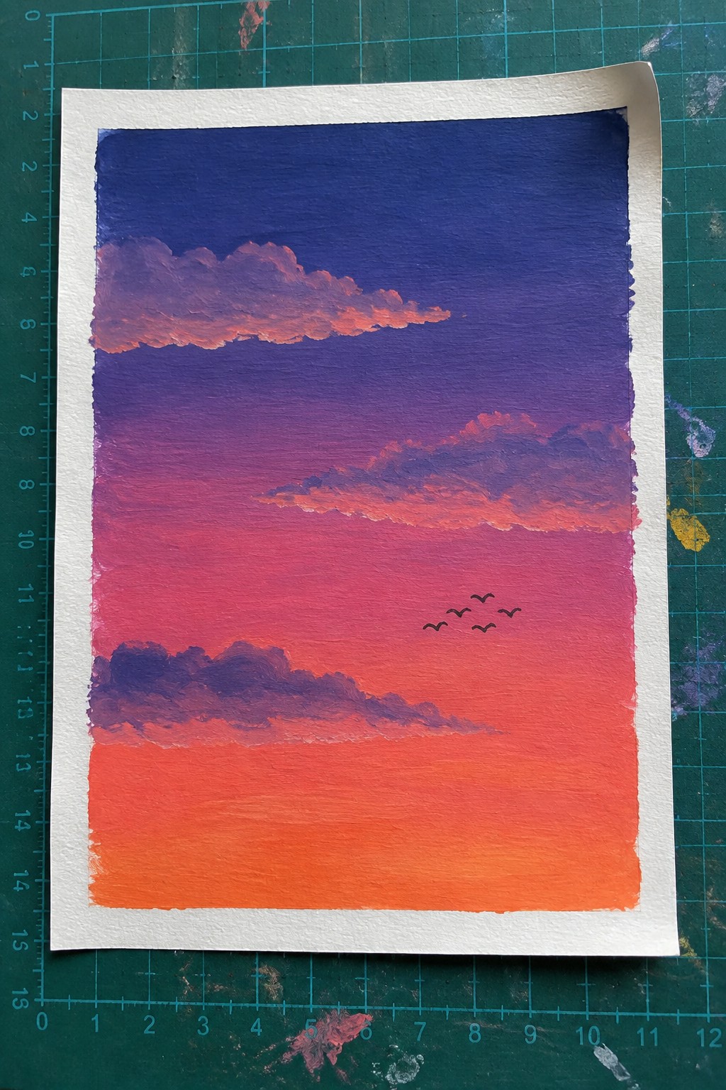 Watercolor sunset sky gradient from blue to orange with pink clouds and birds on green mat