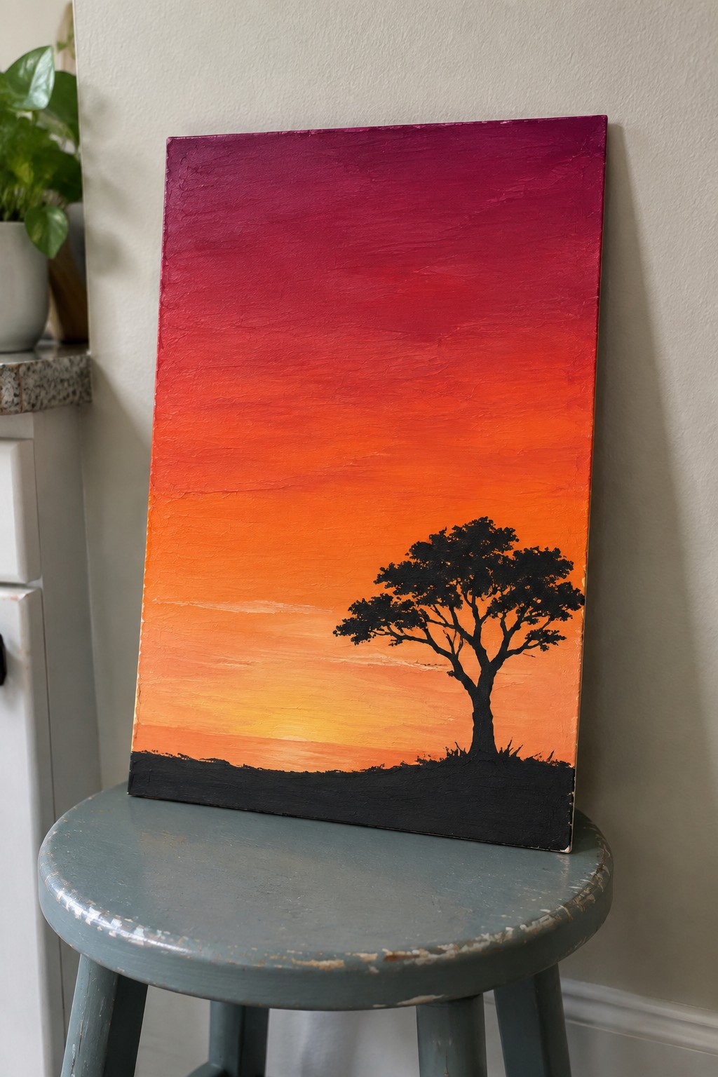 Gradient sunset painting from magenta to yellow with black tree on blue stool