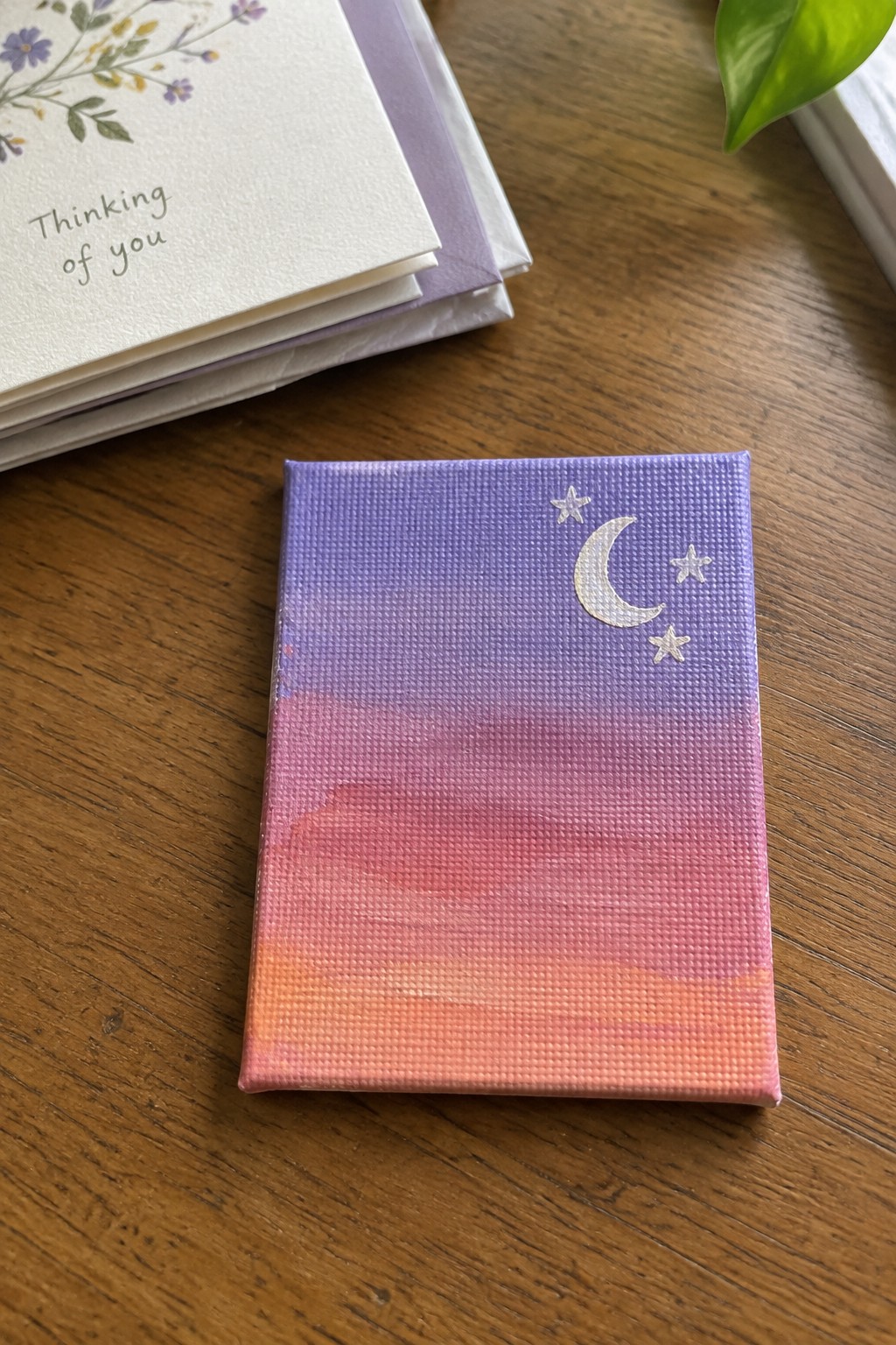 Mini canvas with purple-pink-orange gradient, crescent moon and stars on wooden table beside cards