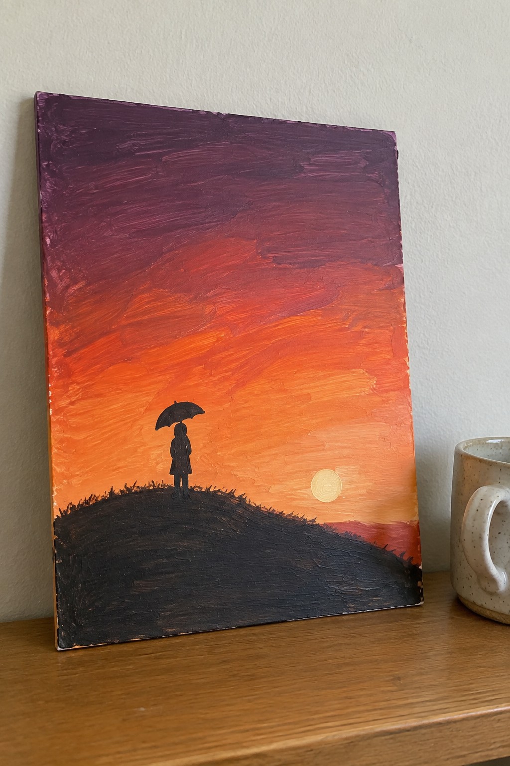Silhouetted person with umbrella on dark hill under red-orange sunset sky