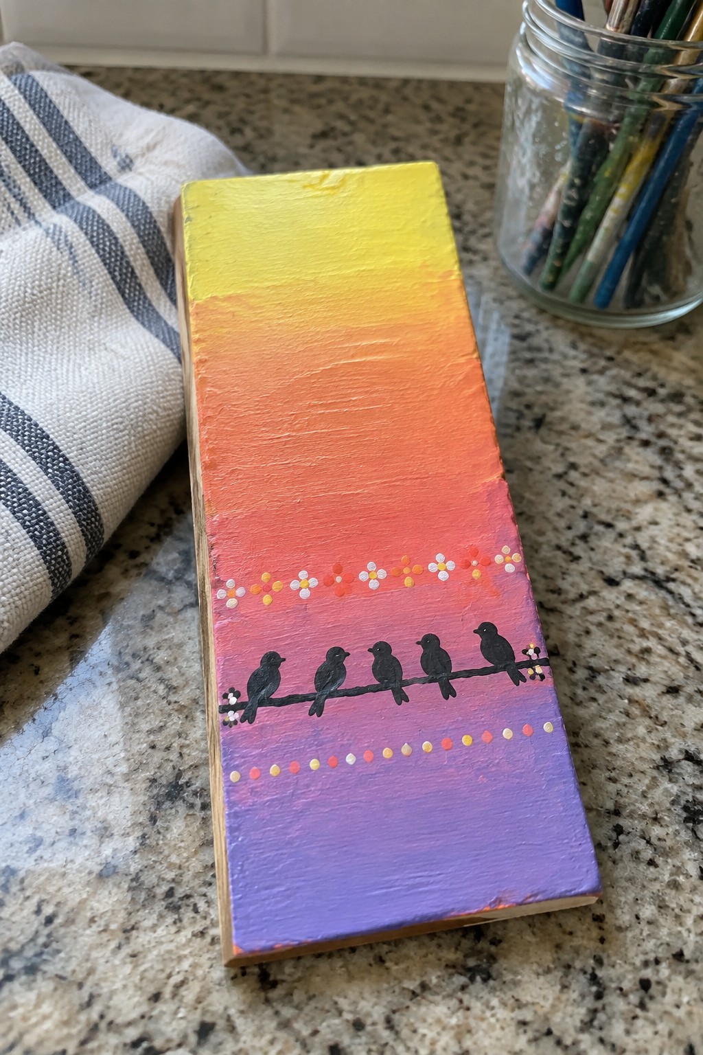 Painted wooden block with yellow-to-purple gradient, five black birds on branch, dotted flowers.