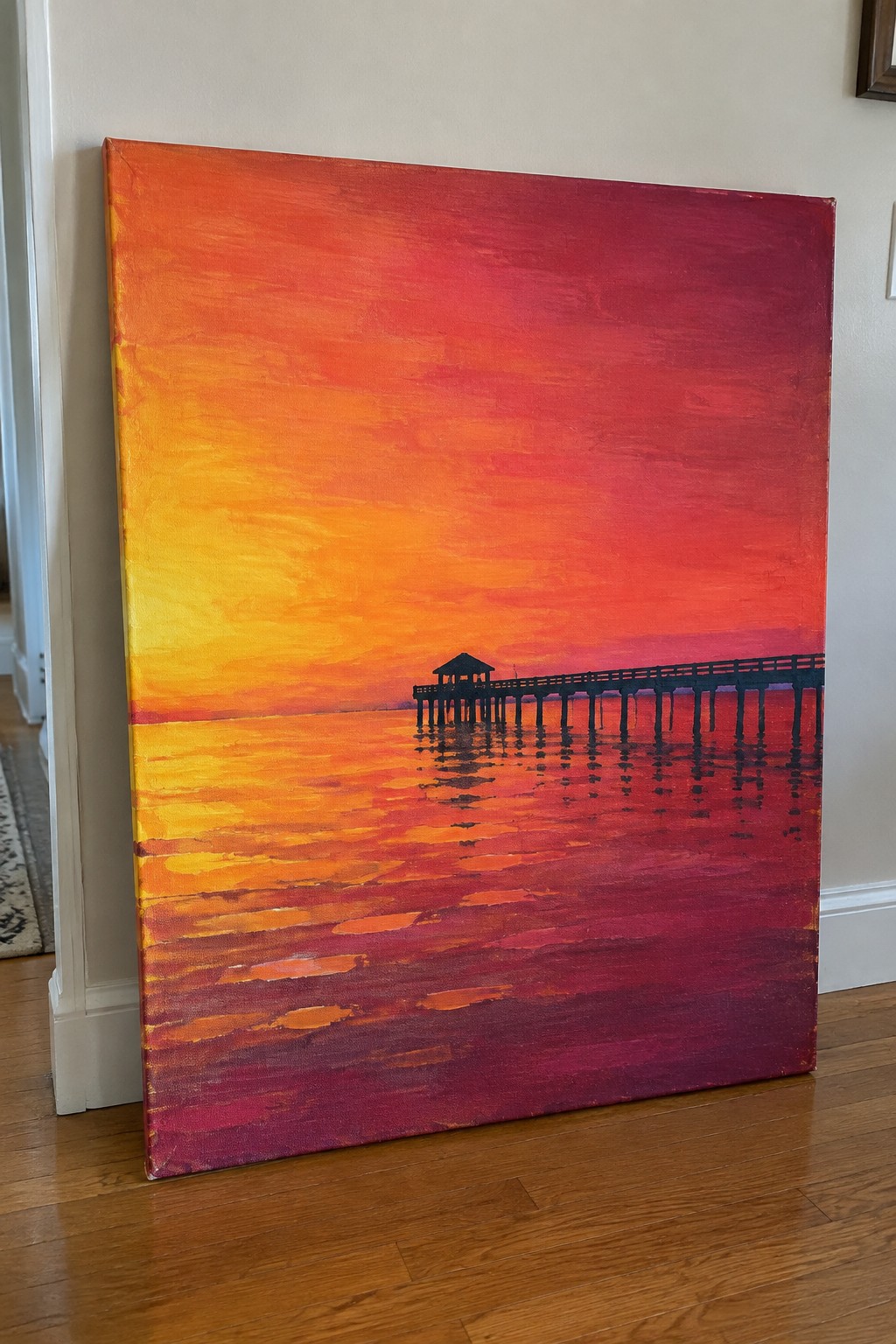Vibrant sunset painting with yellow-orange-red sky and silhouetted pier over reflective water