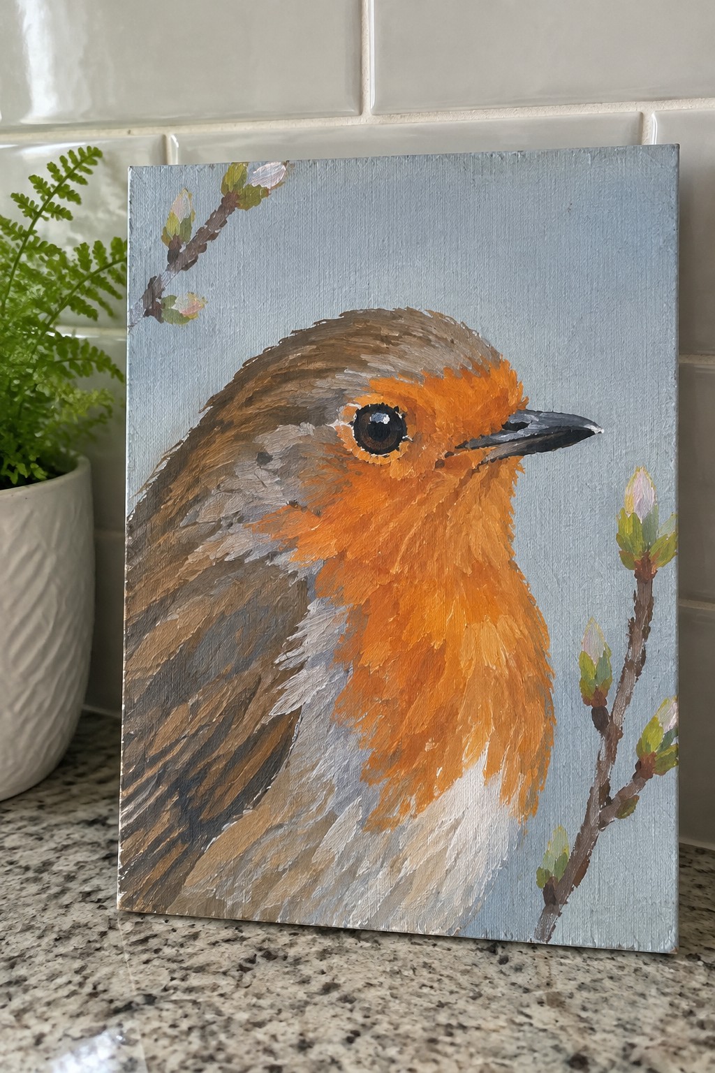Acrylic painting of robin with orange breast on light blue canvas with budding branches