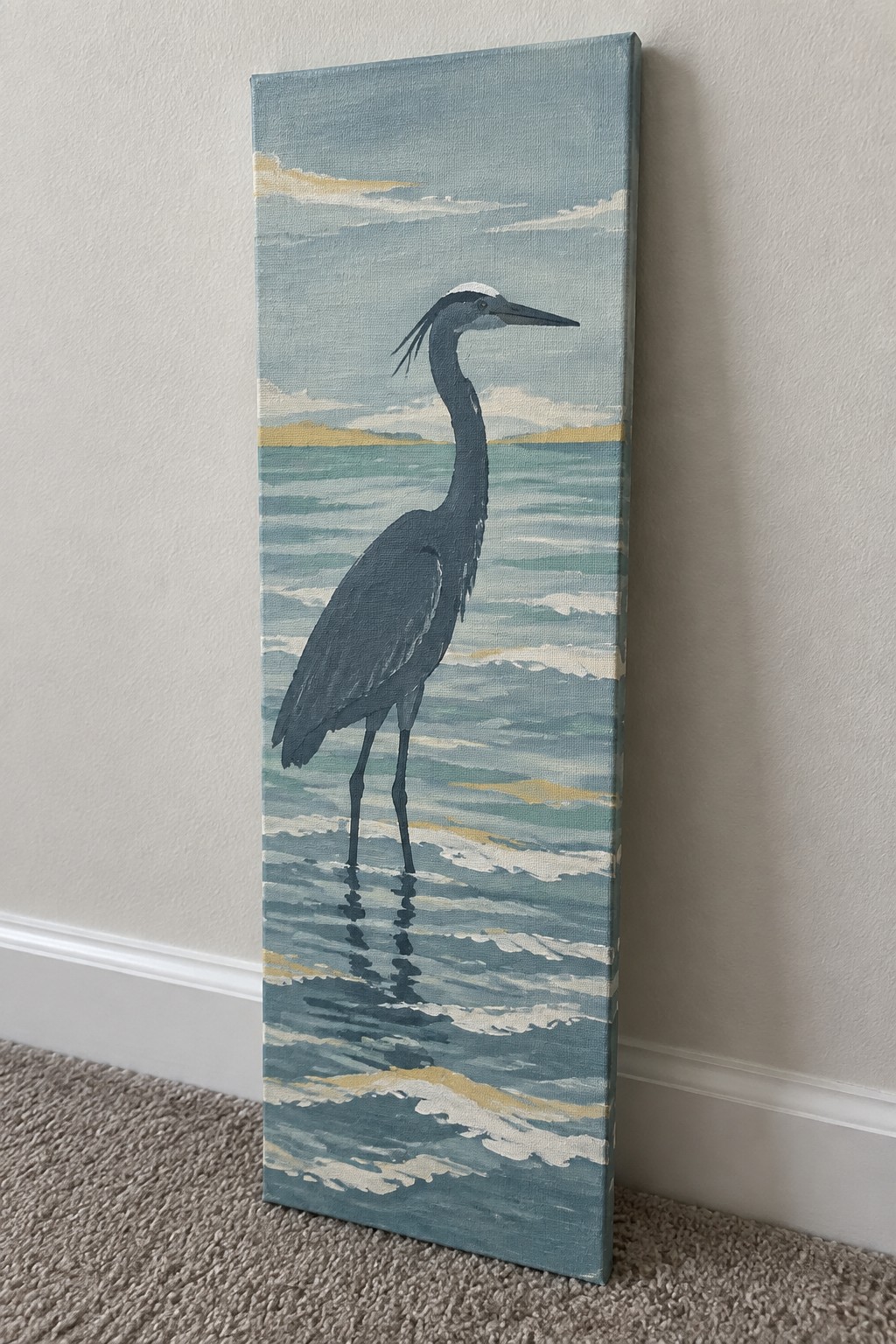 Vertical canvas painting of a heron standing in blue ocean waves leaning on a wall.