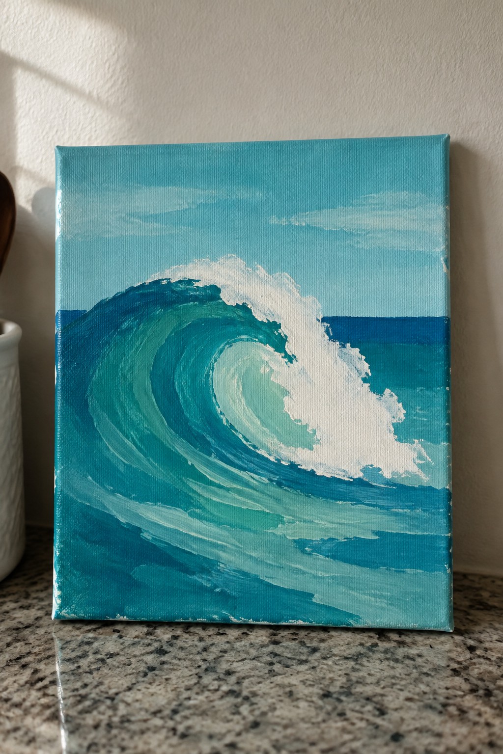 Small canvas painting of curling turquoise wave with white foam on granite countertop.
