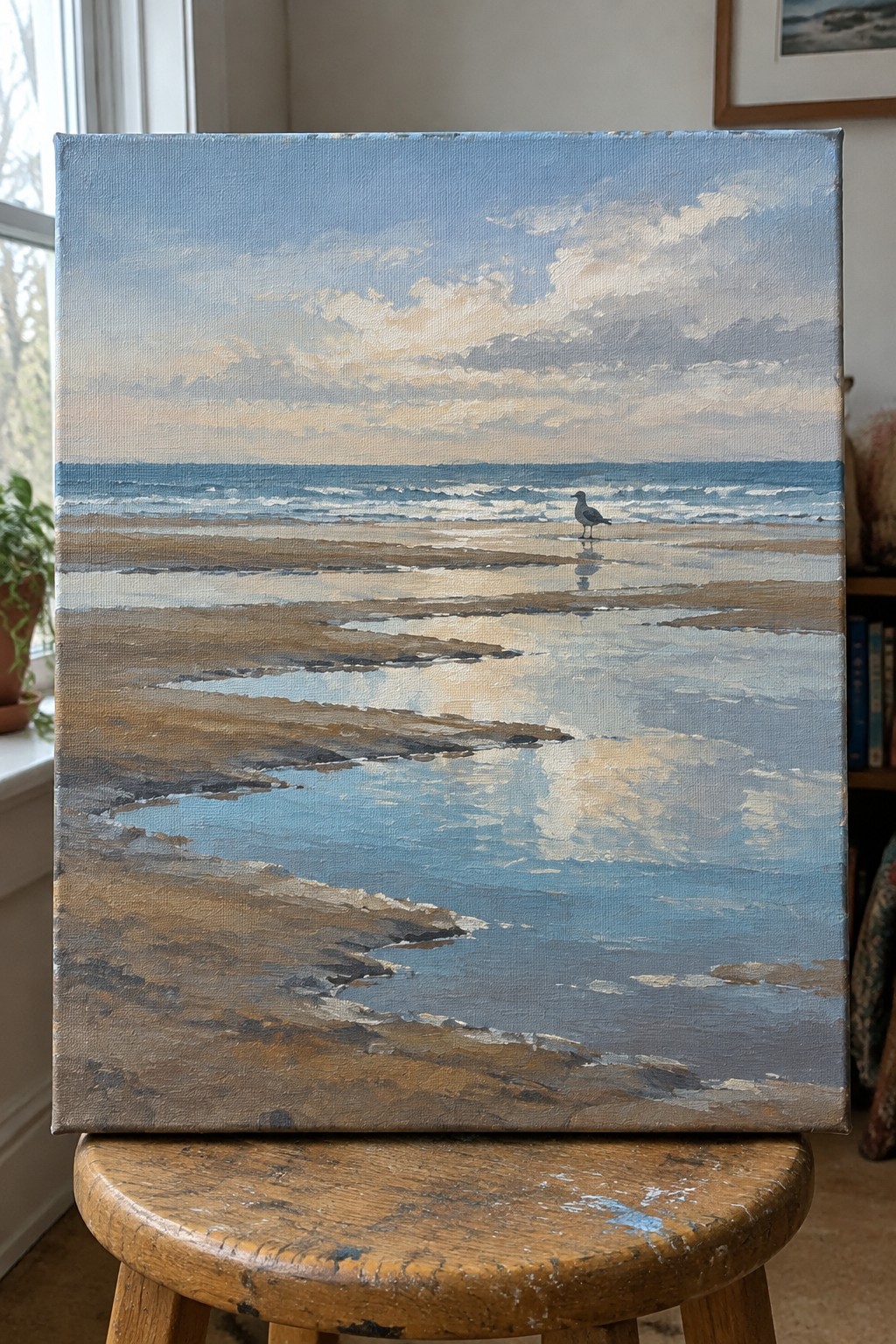 Beach painting with lone seagull on wet sand, propped on wooden stool