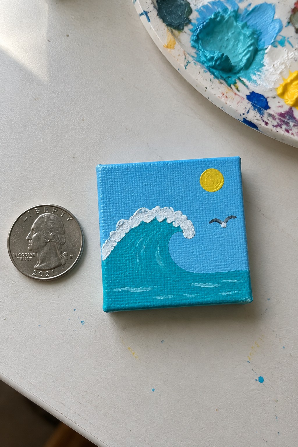 Tiny wave painting on canvas beside a 2021 US quarter coin.