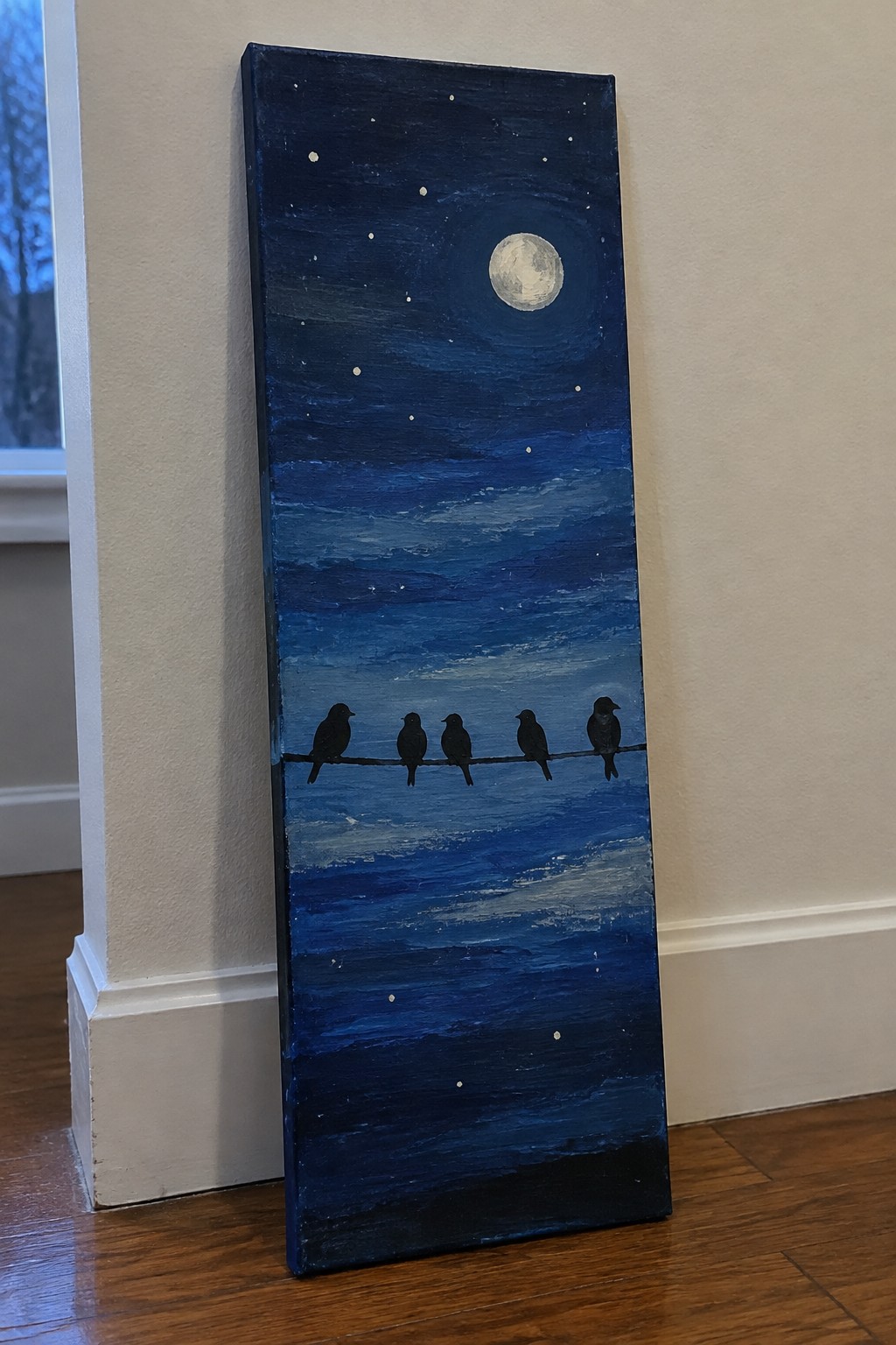 Five silhouetted birds perch on a wire under a full moon in starry blue night sky.