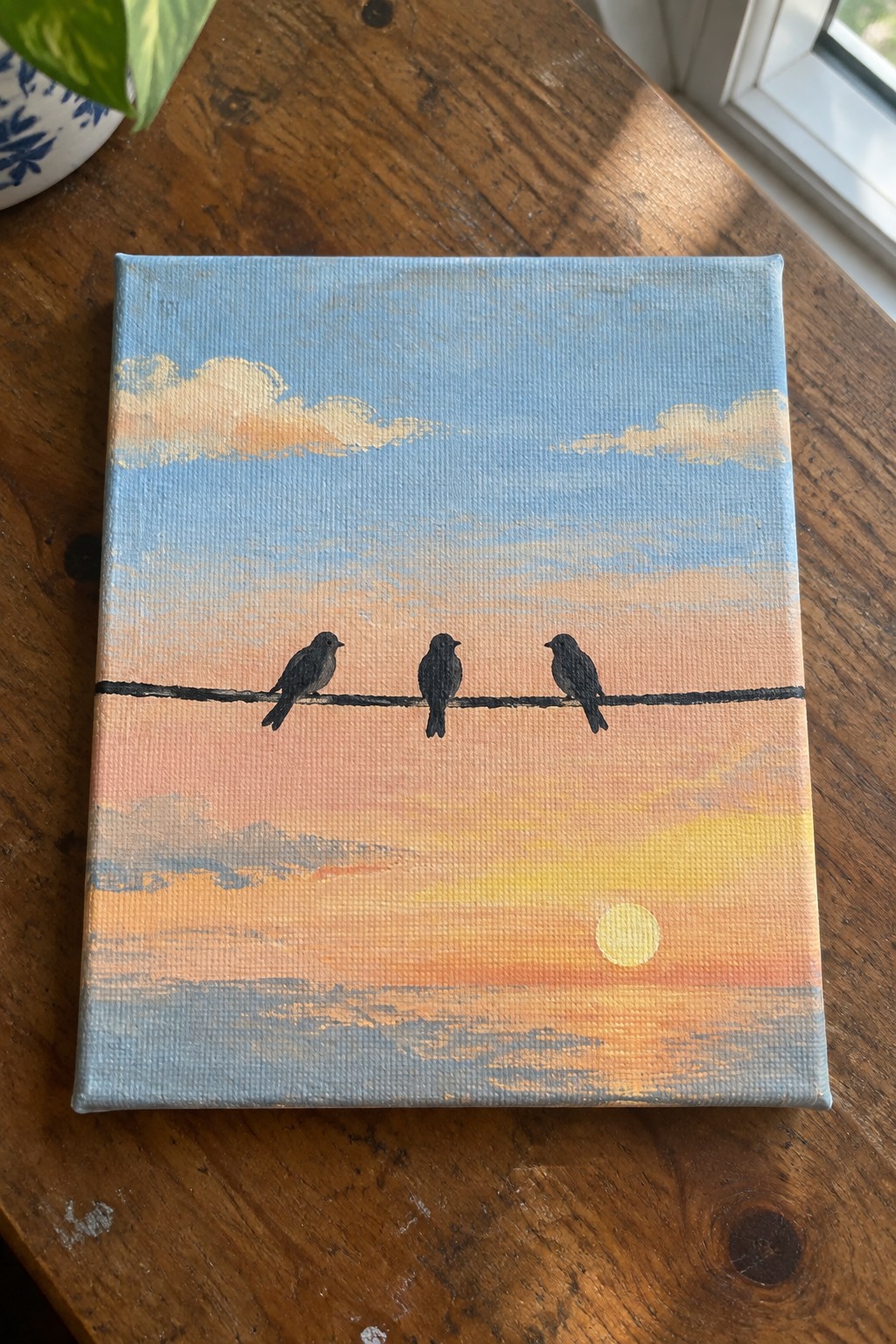 Three black birds perched on wire against gradient sunset sky with sun