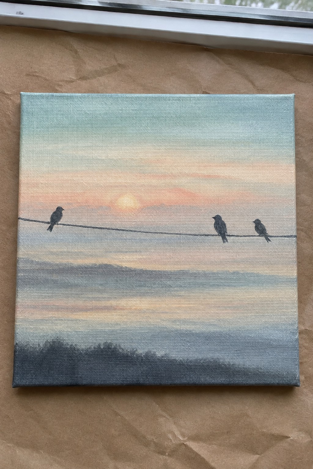 Three silhouetted birds on a wire against a gradient sunset over dark hills.