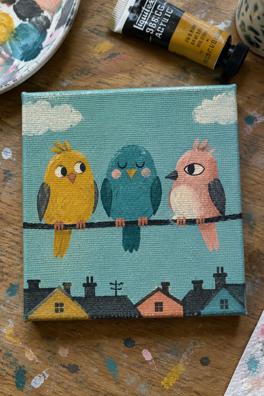 Three cartoon birds on wire above colorful houses on teal canvas with paint supplies