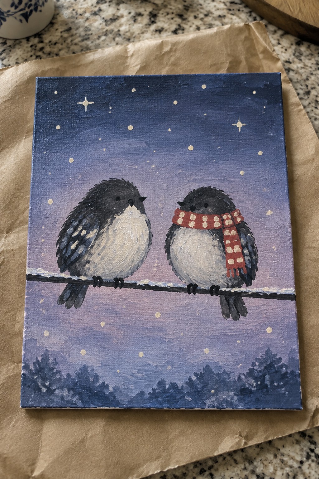 Two birds on snowy wire under starry purple sky, one in red polka-dot scarf.