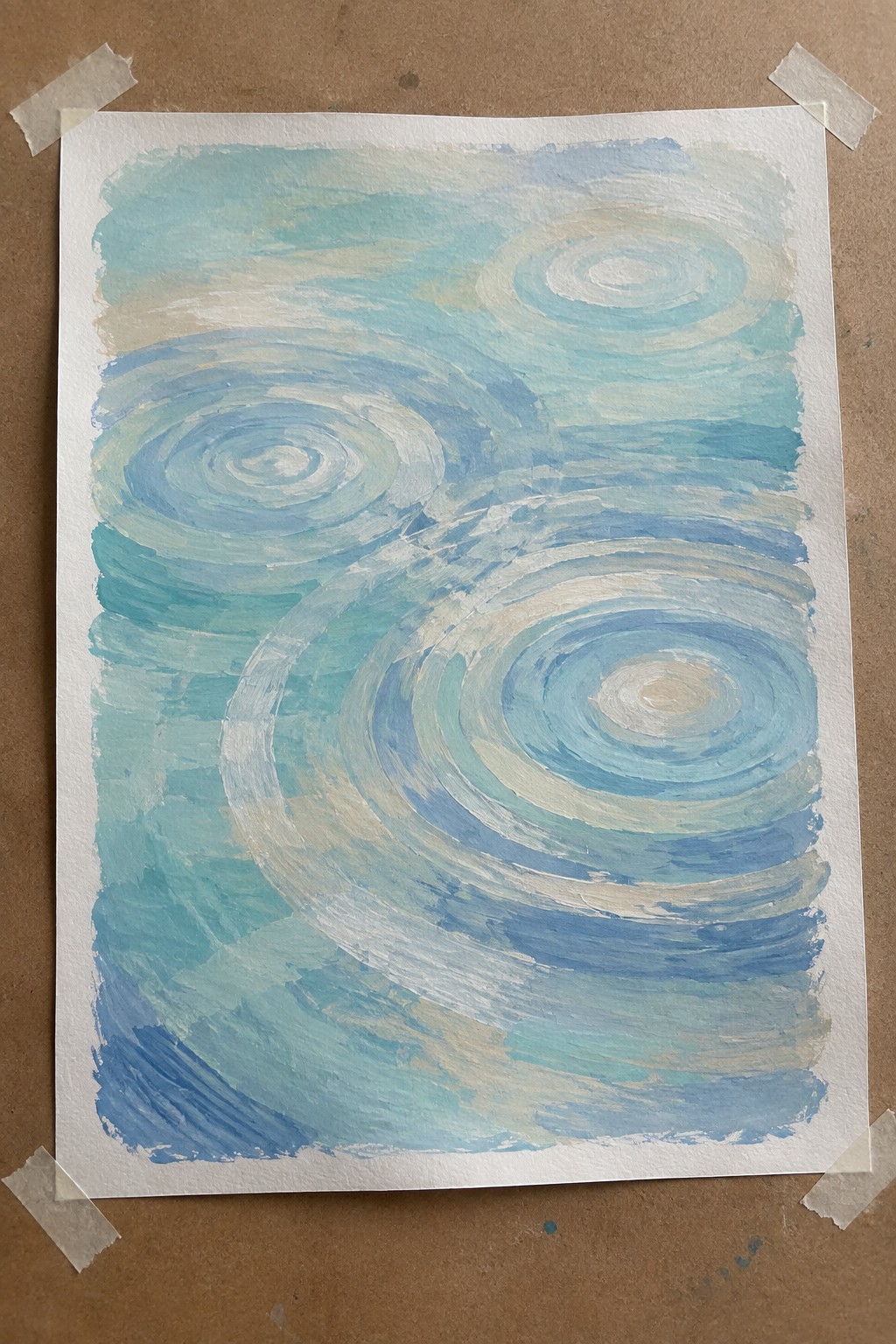Abstract watercolor with blue swirling circles on white paper taped to brown surface.