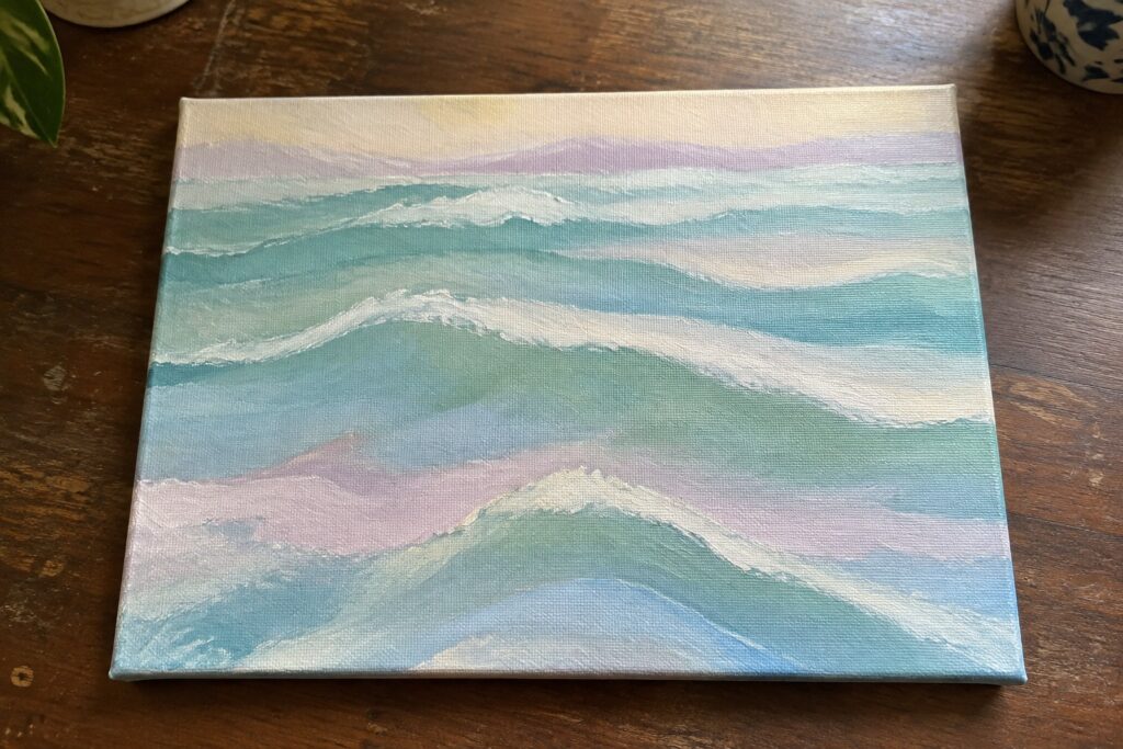 Pastel seascape painting of rolling turquoise waves on wooden table.