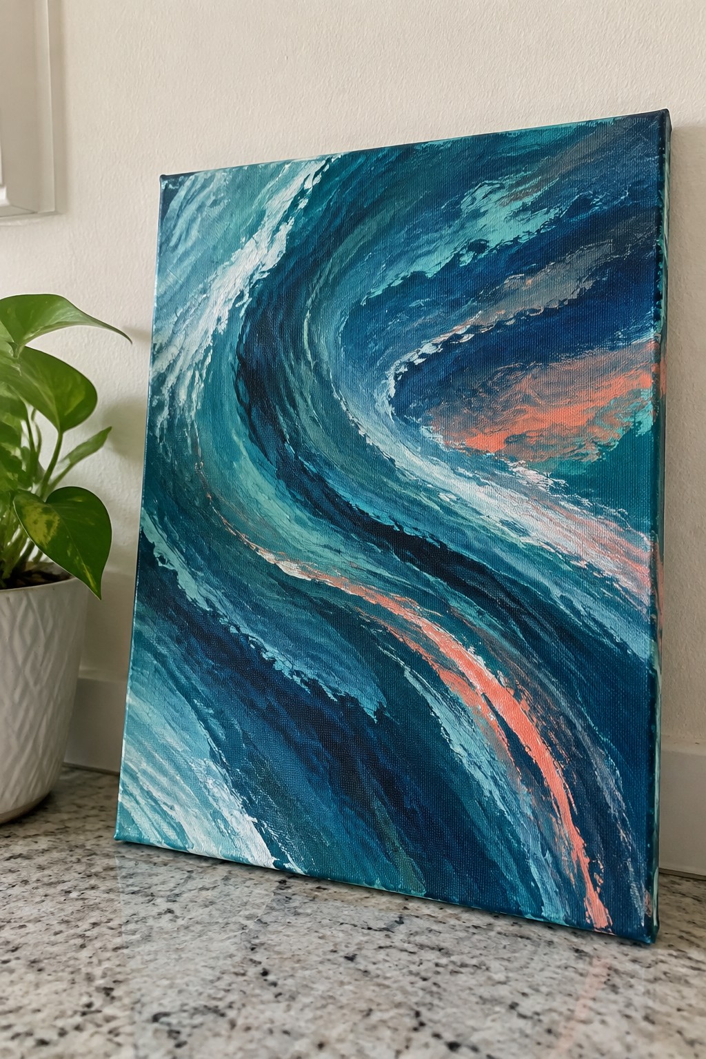 Swirling teal and blue wave painting on canvas beside green potted plant on marble