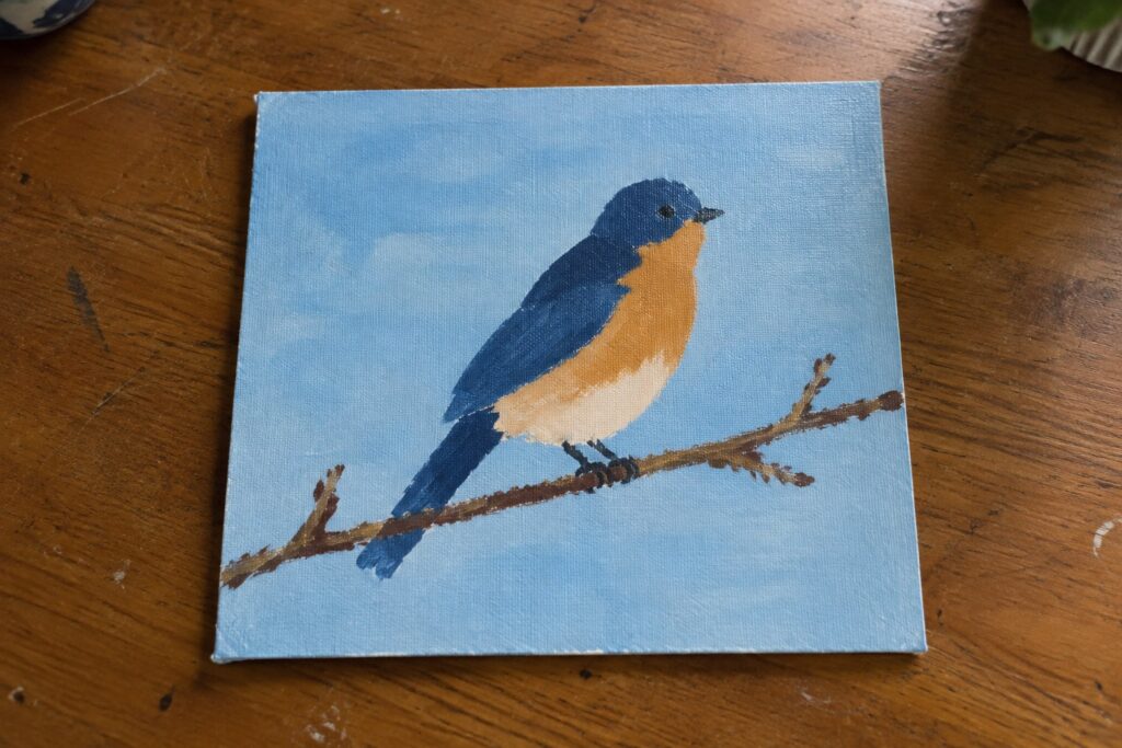 Blue and orange bird painted on canvas perched on branch against light blue background