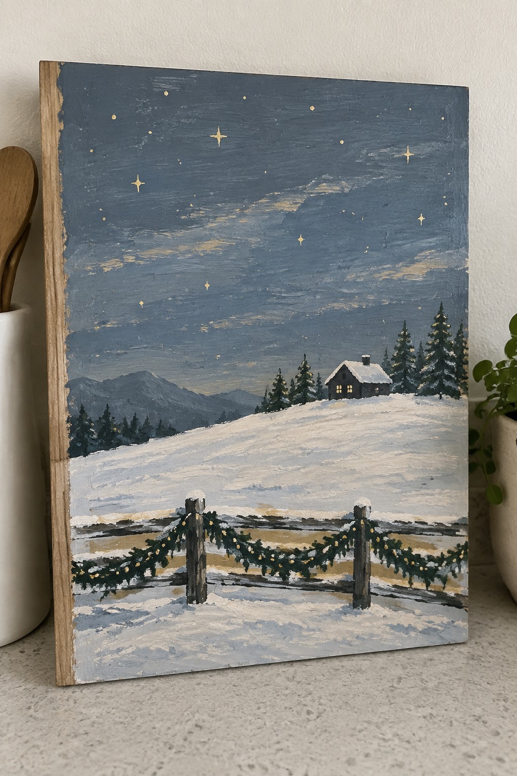 Winter painting of snowy cabin under starry sky with garland fence and mountains